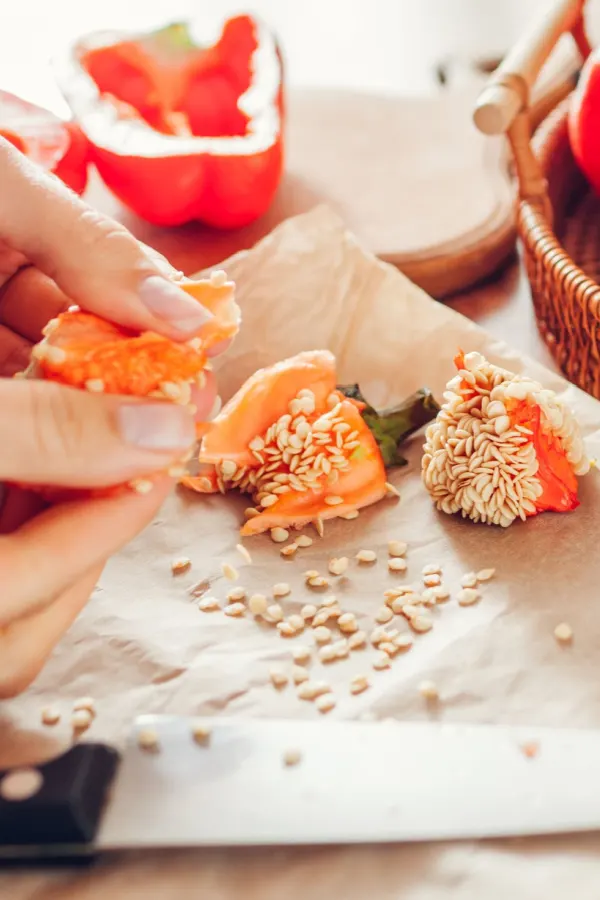 Female fingers removing pepper plant seeds onto a piece of paper.